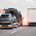 An open car carrier truck next to an enclosed car carrier