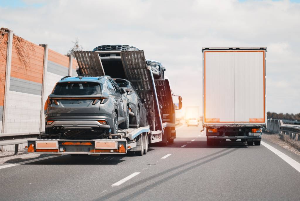 An open car carrier truck next to an enclosed car carrier