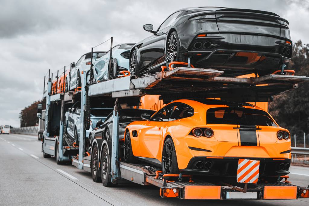 On a two-level hydraulic trailer truck, a load of exotic luxury sport cars gleams with speed and prestige.