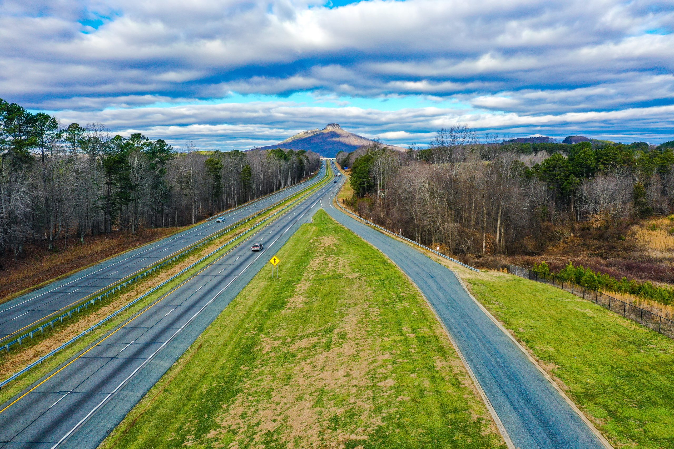 North-Carolina-Aerial-Road-Shot An aerial shot of a road with Pilot mountain in North Carolina, USA and a cloudy blue sky in the background