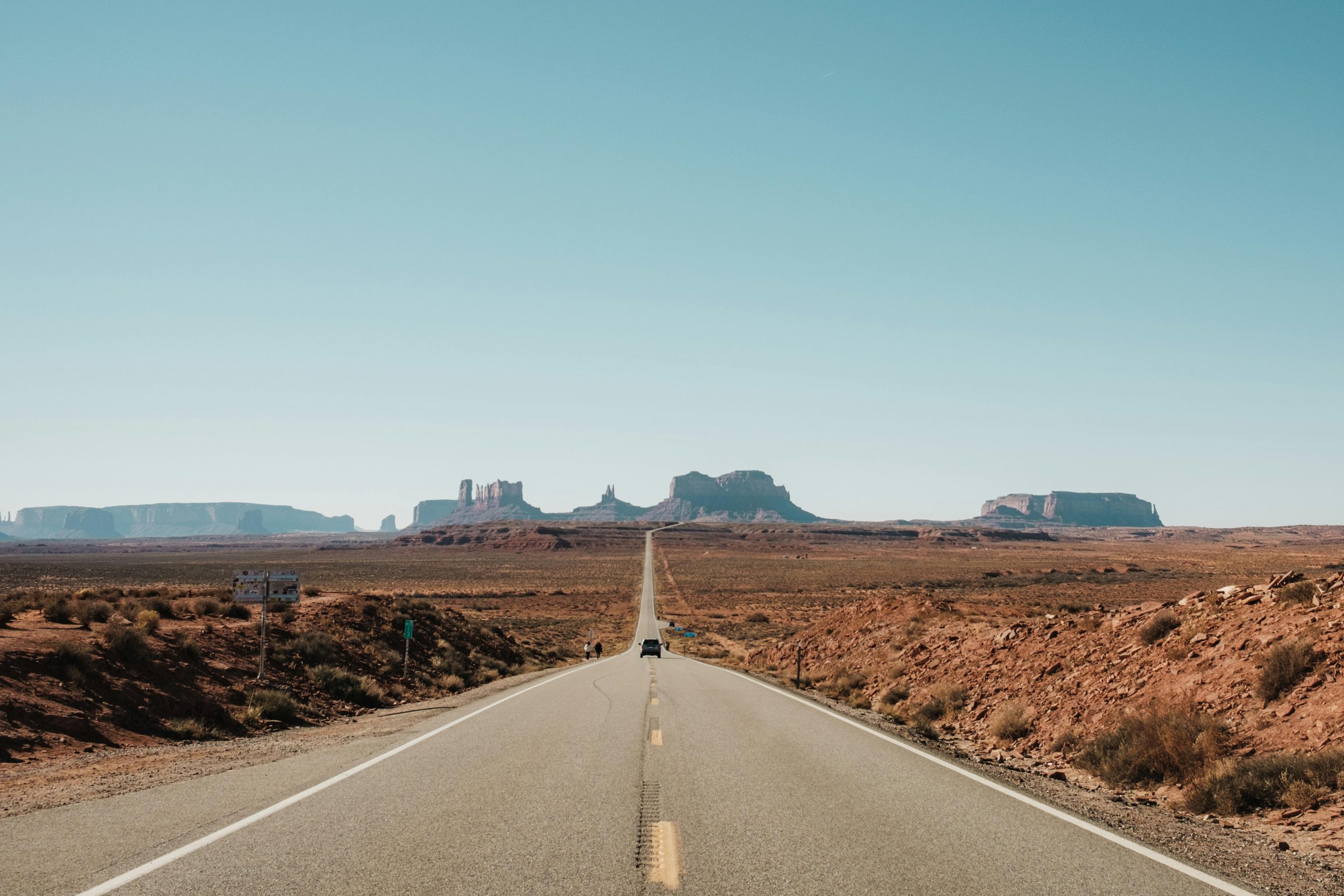 A lone car driving down an endless desert highway towards