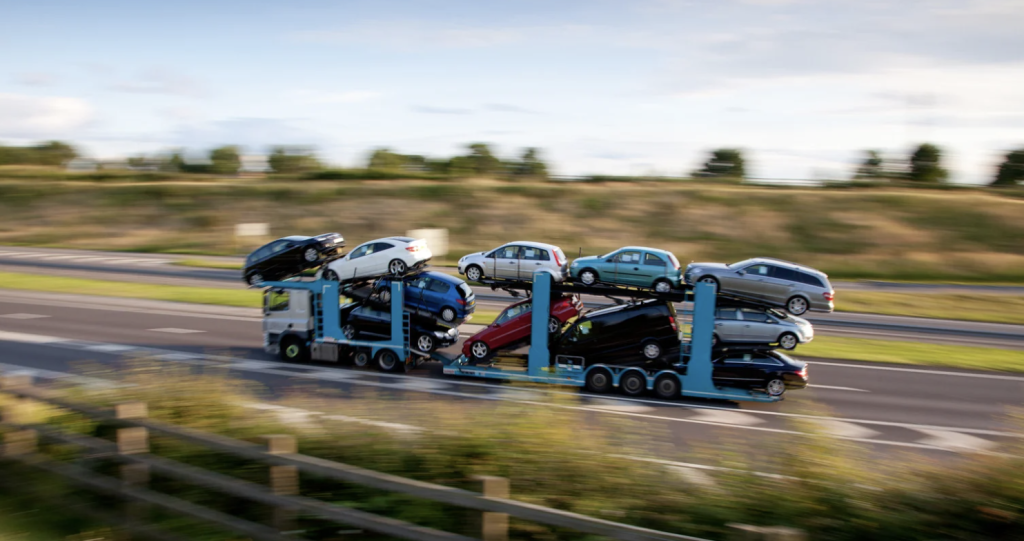 Open carrier auto transport with truck and many cars driving on open freeway with affordable car shipping costs.
