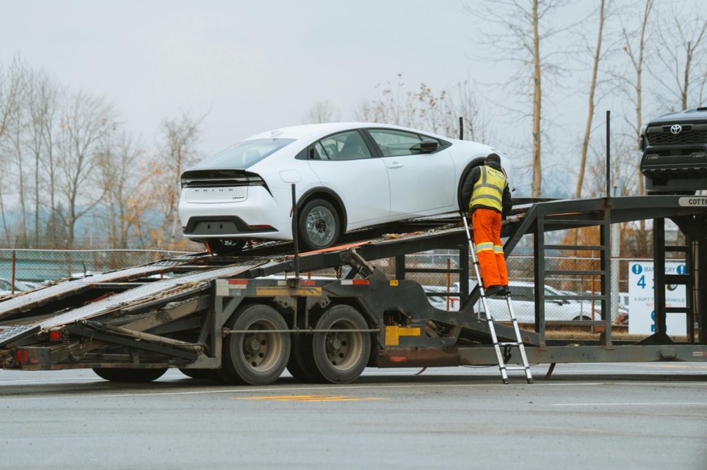 Winter car shipping with man loading white standard car onto transport truck.