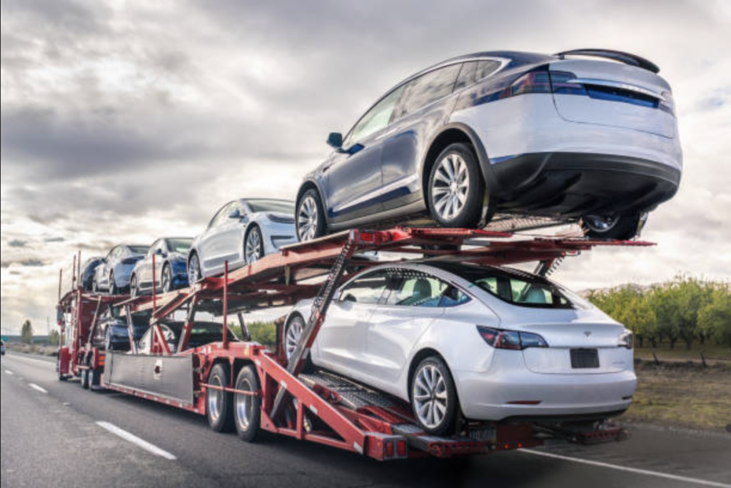 Open carrier hybrid electric car shipping on highway.