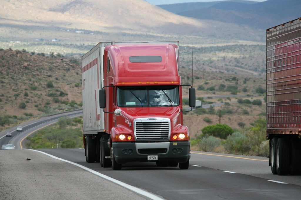 Image of enclosed car shipping semi truck driving on dessert freeway in Arizona