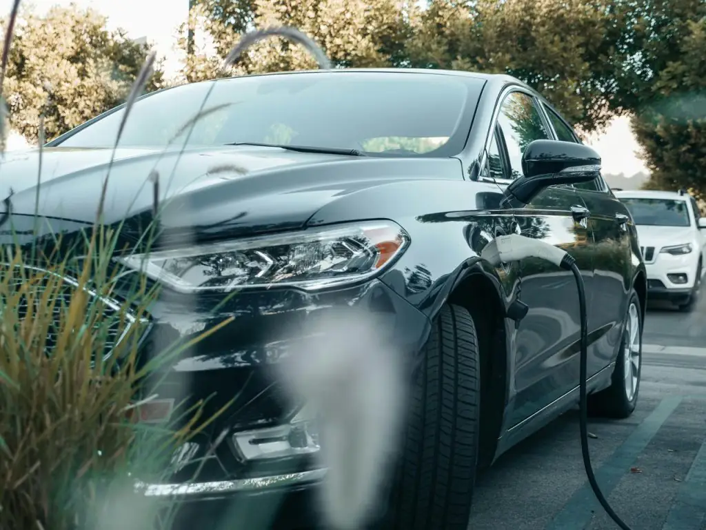 Gray hybrid electric car plugged into charging station.